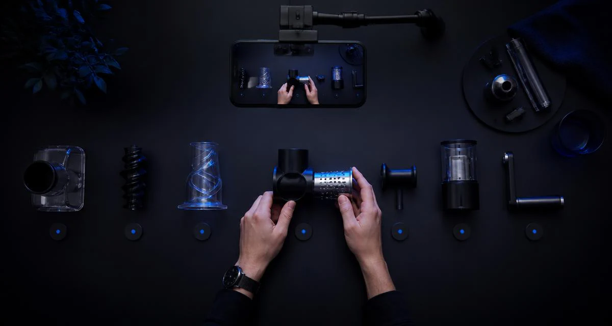 Overhead view of hands assembling a kitchen gadget with parts laid out in a numbered row on a dark counter